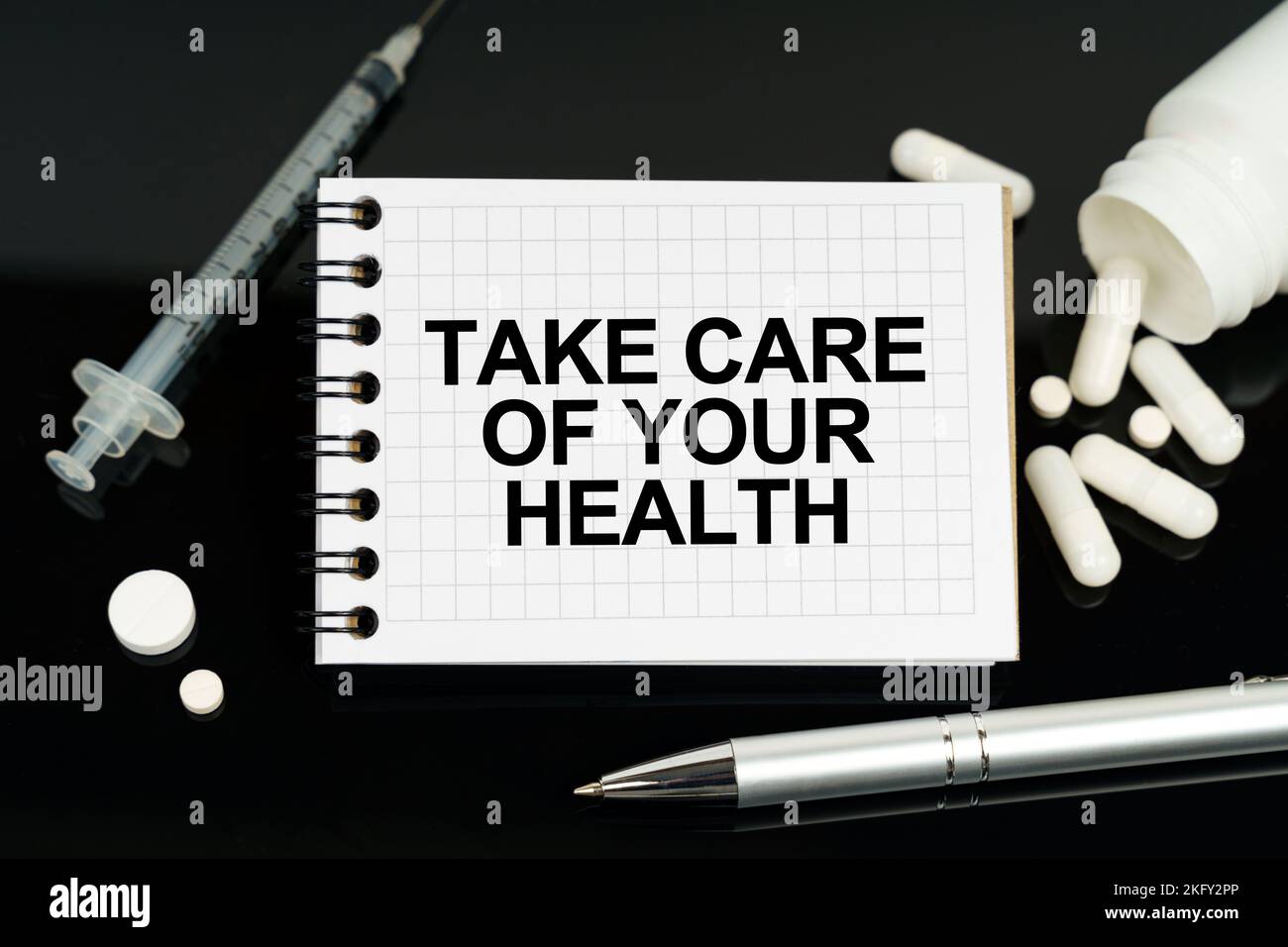 Concetto di medicina e assistenza sanitaria. Sulla superficie nera ci sono pillole, una siringa e un notebook con l'iscrizione - prendersi cura della vostra salute Foto Stock
