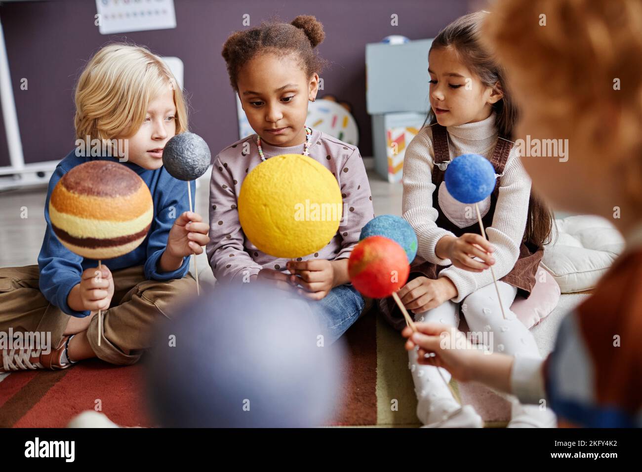 Simpatici piccoli studenti della scuola elementare con modelli di pianeti del sistema solare che discutono le loro caratteristiche mentre studiano l'astronomia Foto Stock
