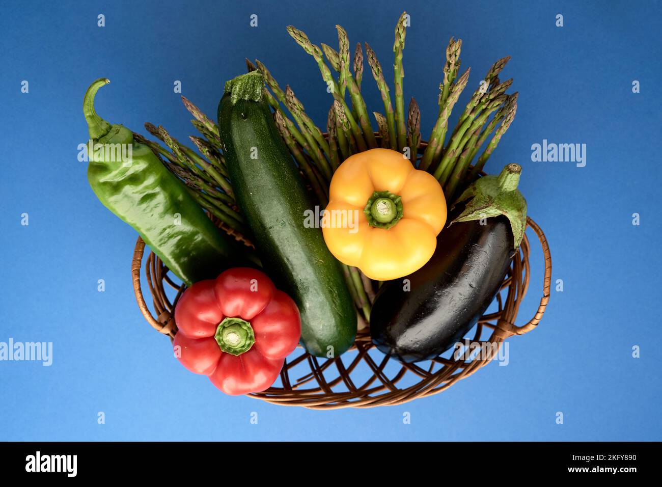 primo piano di un cesto di vimini pieno di verdure su sfondo blu Foto Stock