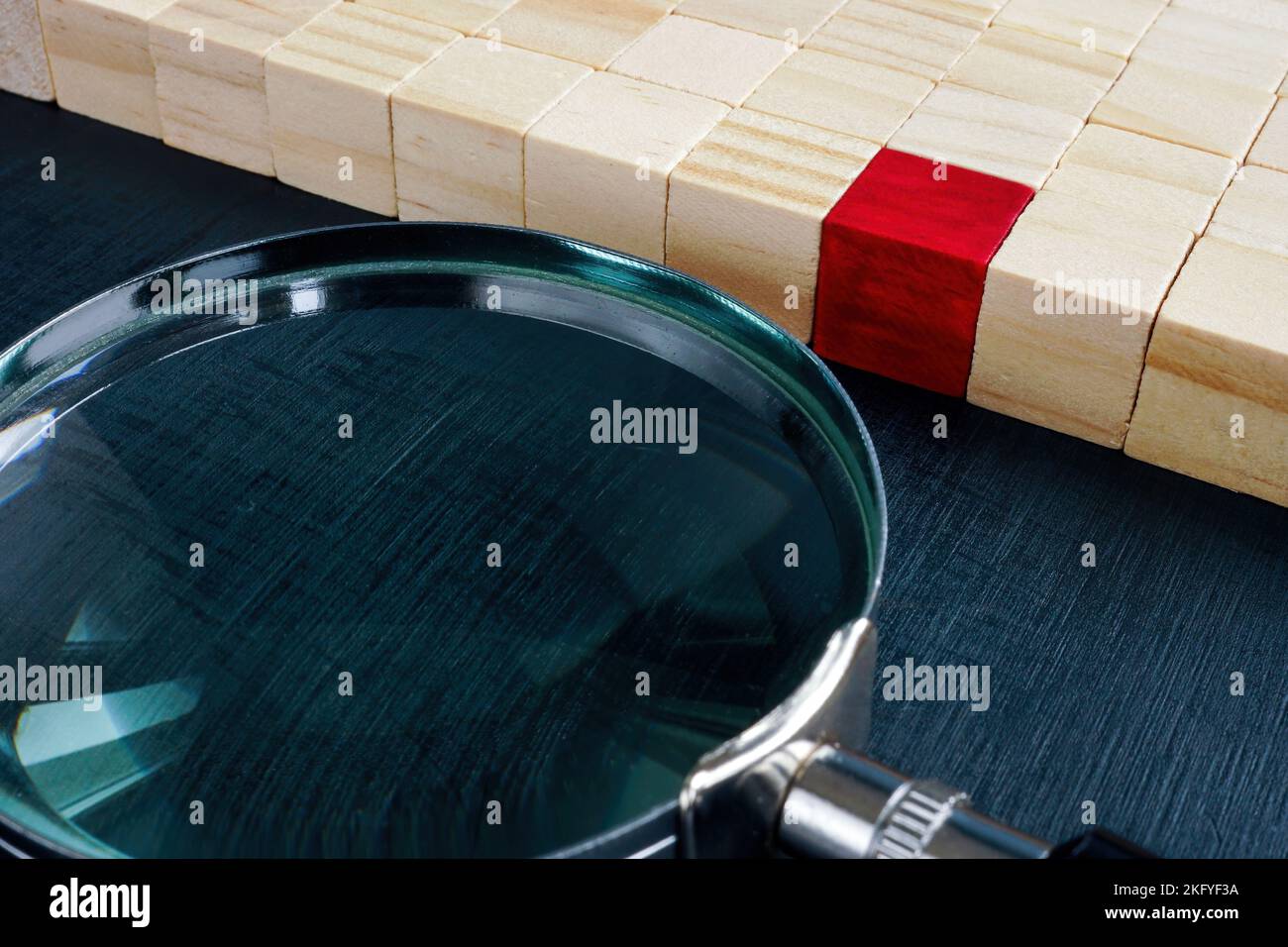Cubetti di legno e uno rosso accanto a una lente d'ingrandimento. Concetto di acquisizione di talenti. Foto Stock