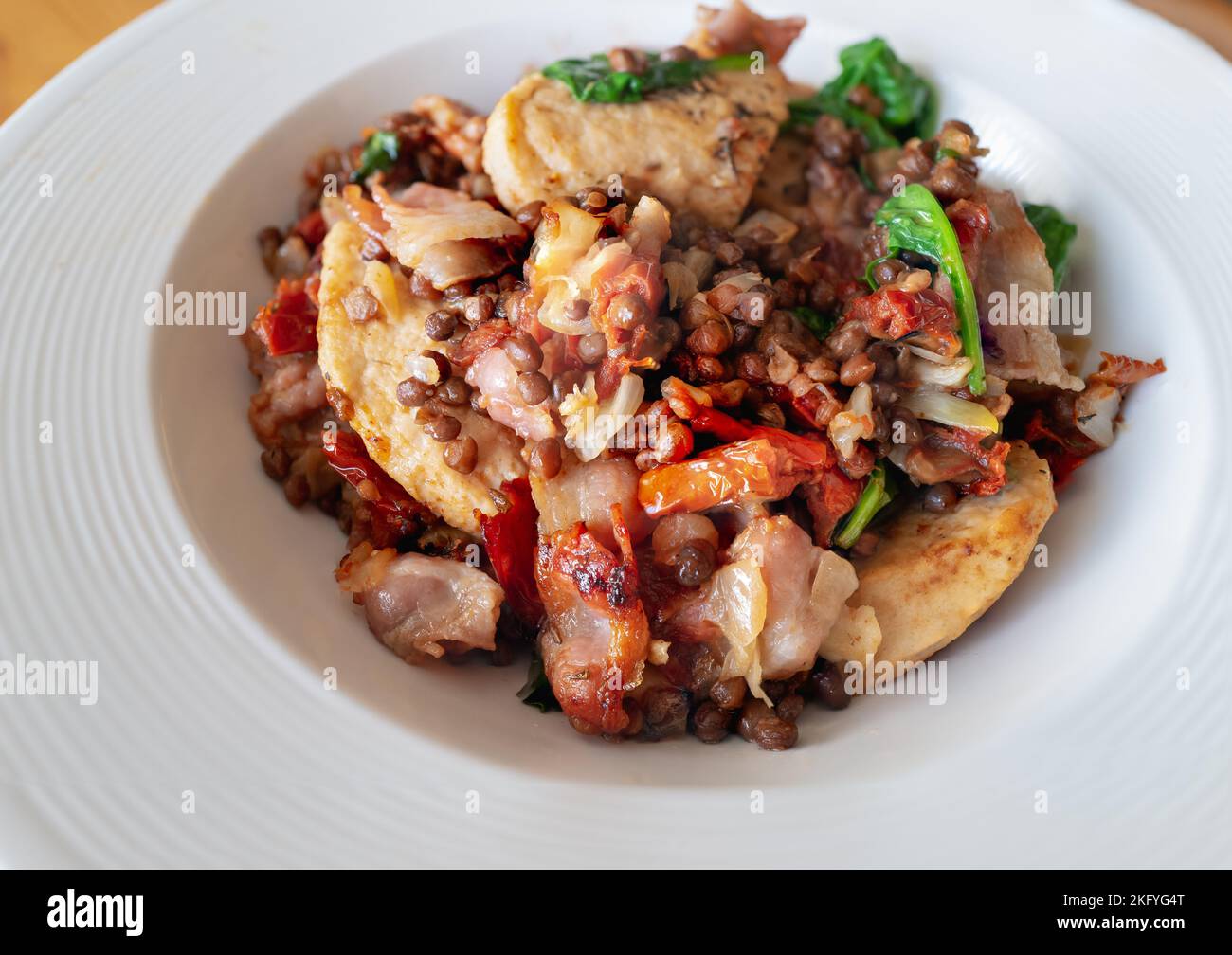 Filetti di pollo di soia con pancetta in un piatto con include anche spinaci, cipolle, lenticchie e pomodori secchi. Foto Stock