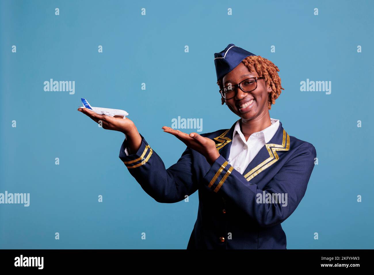 Sorridente afroamericano che indica l'aeroplano commerciale che tiene in mano per la pubblicità della linea aerea. Assistente di volo che indossa l'uniforme dei membri dell'equipaggio nella foto in studio. Foto Stock
