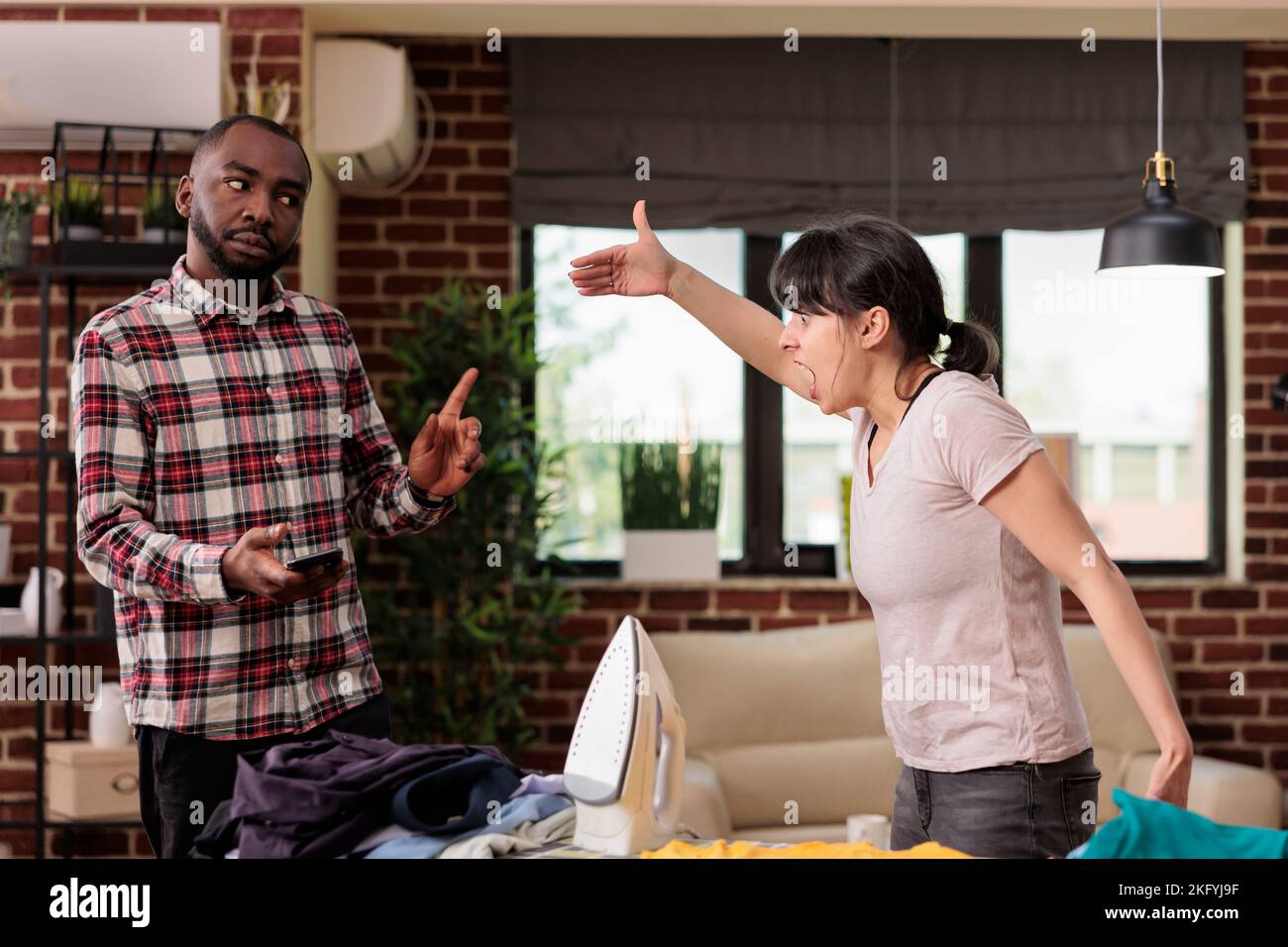 Coppia multirazziale che ha un grande argomento a casa, urla e discutere su questioni irrisolte nel matrimonio. Donna che si lamenta perché il marito afroamericano usa solo il telefono senza aiutare. Foto Stock