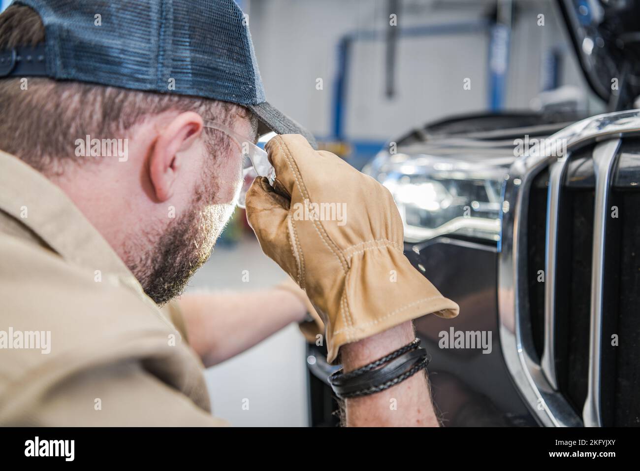 Meccanico caucasico professionista che esegue il controllo dei fari del veicolo durante l'ispezione programmata del veicolo. Tema automobilistico. Foto Stock