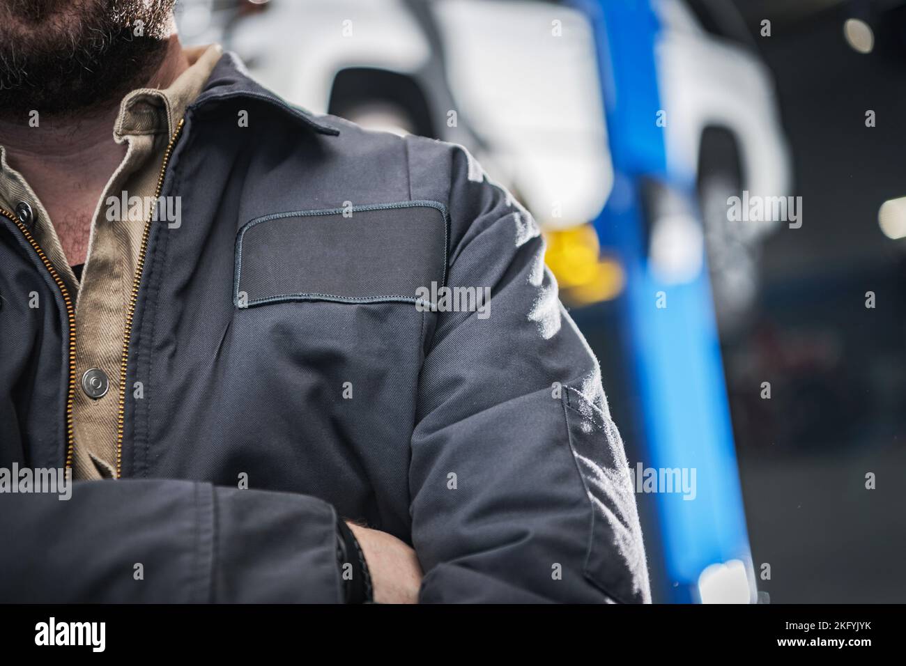 Primo piano di un meccanico caucasico professionale che indossa una giacca da lavoro grigia con copy space patch per il logotipo. Foto Stock