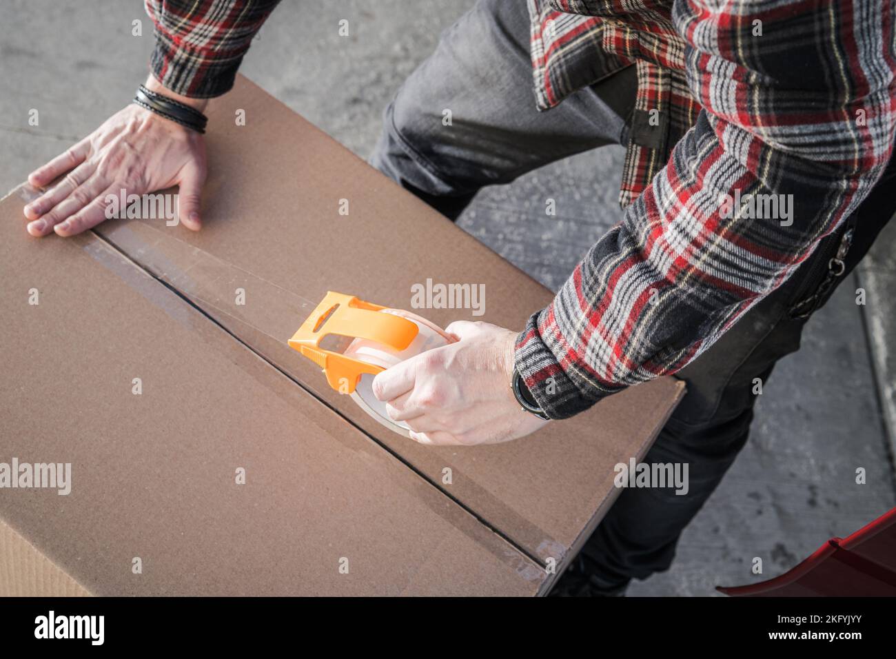 Primo piano di un mover sigillatura di una scatola di cartone con nastro adesivo trasparente. Servizi di movimentazione professionale. Vista aerea. Foto Stock