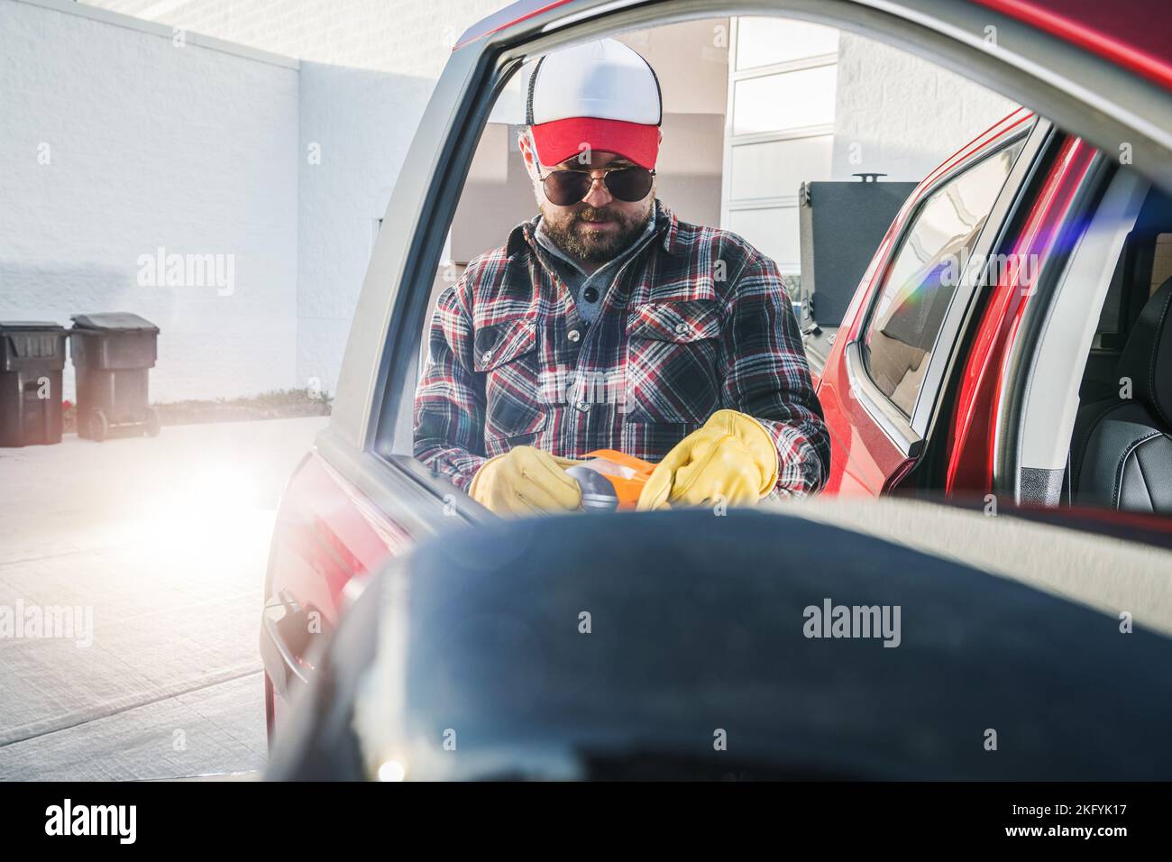 Lavoratore dell'industria automobilistica caucasica di mezza età in piedi accanto alla porta aperta del camion del raccoglitore rosso. Foto Stock
