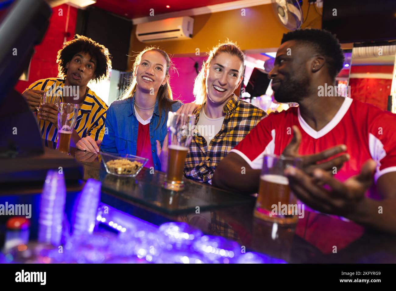 Gruppo di amici maschi e femmine entusiasti che guardano una partita sportiva e parlano in un bar Foto Stock
