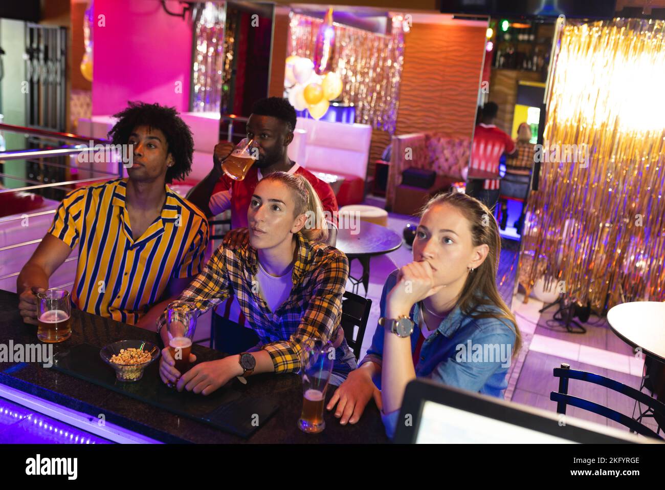Quattro amici maschi e femmine, diversi e tesi, che guardano una partita di sport in un bar Foto Stock
