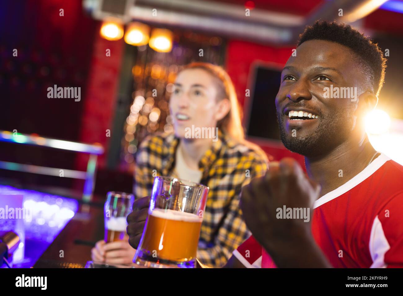 Amico maschile e femminile diversificato ed entusiasta che reagisce ai giochi sportivi che si esibire in un bar Foto Stock