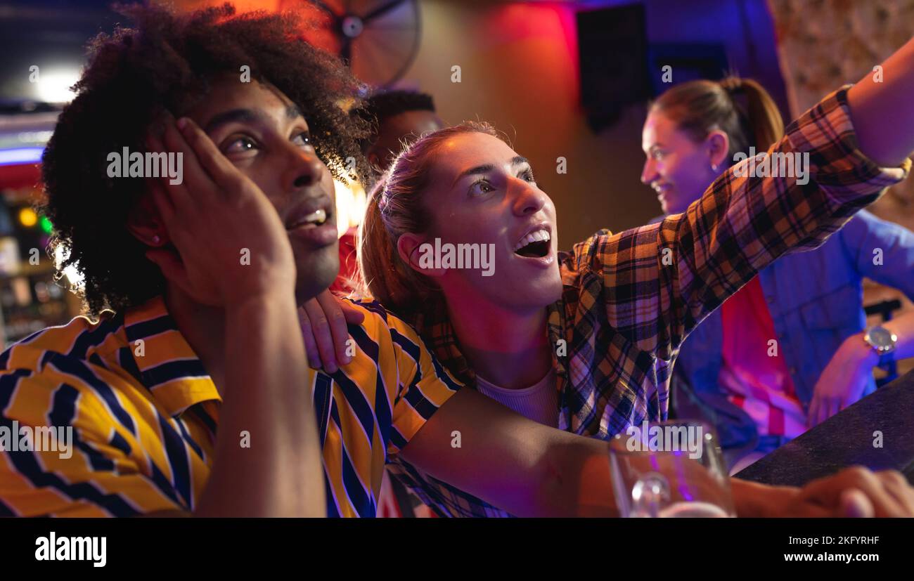 Gruppo di amici maschi e femmine entusiasti che guardano una partita di sport in un bar Foto Stock