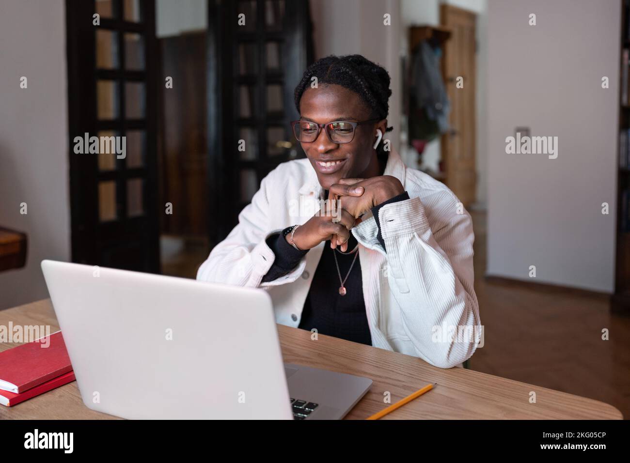 Un uomo afroamericano di ispirazione allegra che sorride guardando lo schermo del computer portatile siede al tavolo dell'appartamento Foto Stock