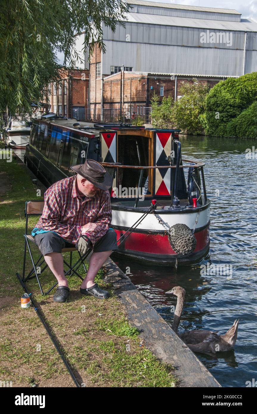 L'operatore di un narrowboat si rilassa sulla riva accanto alla sua nave, ormeggiata nel Tamigi a Osney Island, Oxford, Inghilterra Foto Stock