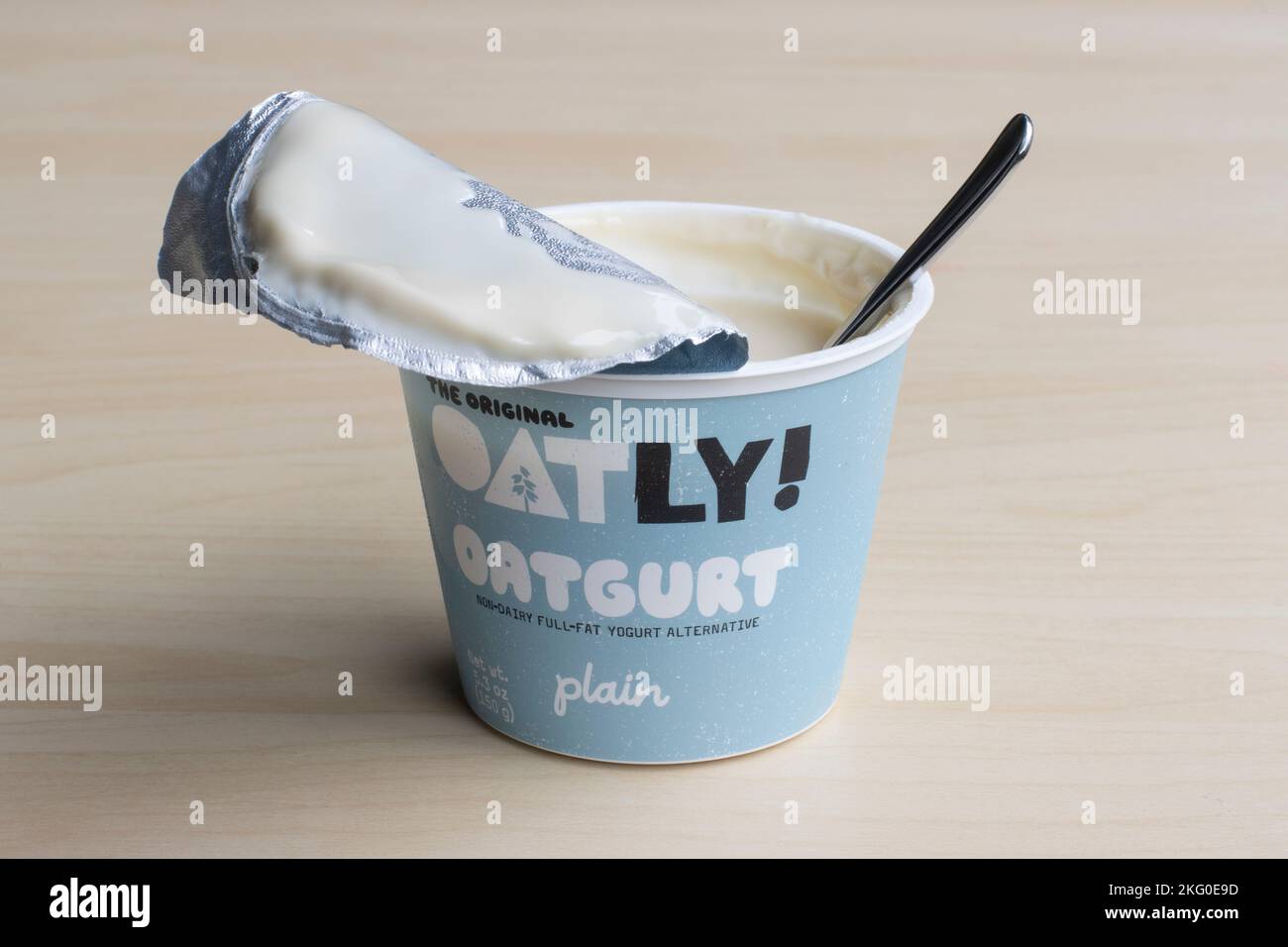 Una tazza di oatgurt semplice di marca Oatly, un'alternativa di yogurt intero non caseario prodotta da Oatly Group AB, con un cucchiaio, isolato su fondo di legno. Foto Stock