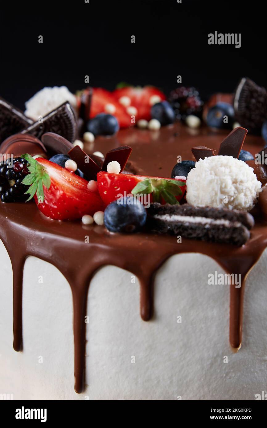 Torta di compleanno su sfondo scuro. Primo piano di torta decorata con frutti di bosco freschi e dolci al cioccolato su sfondo scuro. Delizioso dessert per la festa Foto Stock