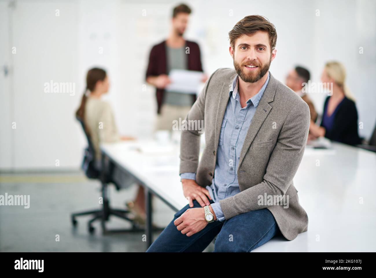 HES una giovane pistola in azienda. Ritratto di un giovane uomo d'affari in ufficio con colleghi sullo sfondo. Foto Stock