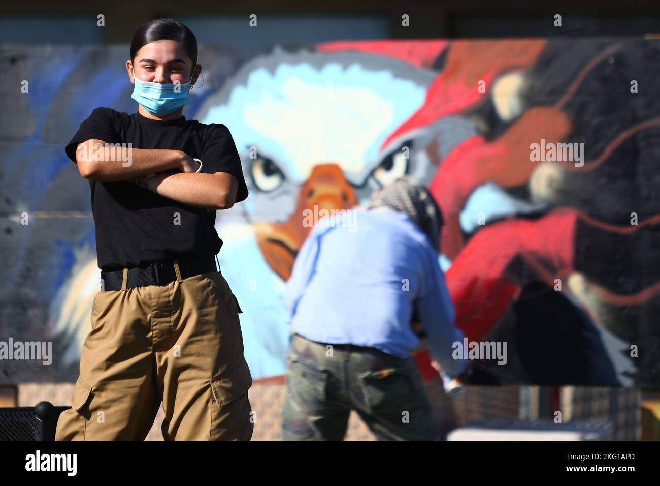 Sunburst Youth Challenge Academy Class 30 Cadet Noemi Herrera posa all'inizio di una danza hip-hop mentre un artista graffiti crea un murale patriottico sullo sfondo durante una vetrina di performance dei Beats Lyrics leader, 21 ottobre 2022, presso la Joint Forces Training base, Los Alamitos, California. I cadetti hanno trascorso la settimana immersi nell'educazione artistica con guide di arte visiva, musica e danza di Beats Lyrics. Il programma mirava ad aprire gli studenti alle arti come meccanismo di coping e percorso verso l'espressione di sé. Sunburst è un programma di recupero crediti delle scuole superiori, gestito in collaborazione con il Califo Foto Stock