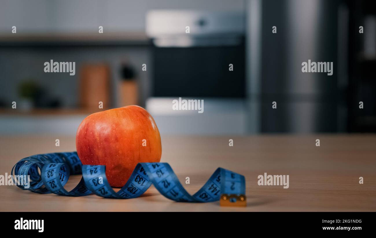 Mela rossa e metro a nastro sul tavolo da cucina in primo piano sfocato uomo africano sullo sfondo ragazzo apertura frigorifero frigorifero alla ricerca di cibo per mangiare Foto Stock