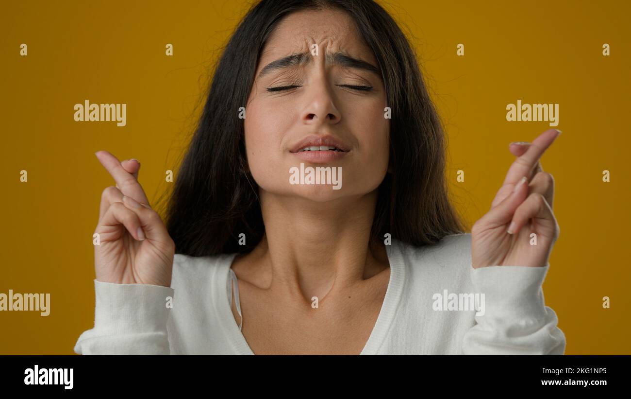 Primo piano ritratto in studio sfondo giallo indiano etnia donna ragazza donna femmina rende desiderio croci dita per buona fortuna attende desiderio di pregare Foto Stock