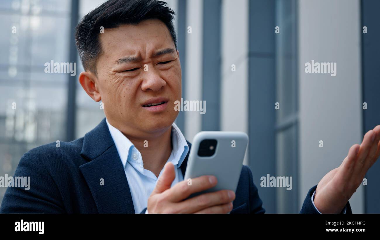 Primo piano asiatico di mezza età uomo adulto pazzo infelice uomo d'affari sentirsi infastidito con l'uso di smartphone rotto problema batteria scarica arrabbiato avere problema Foto Stock