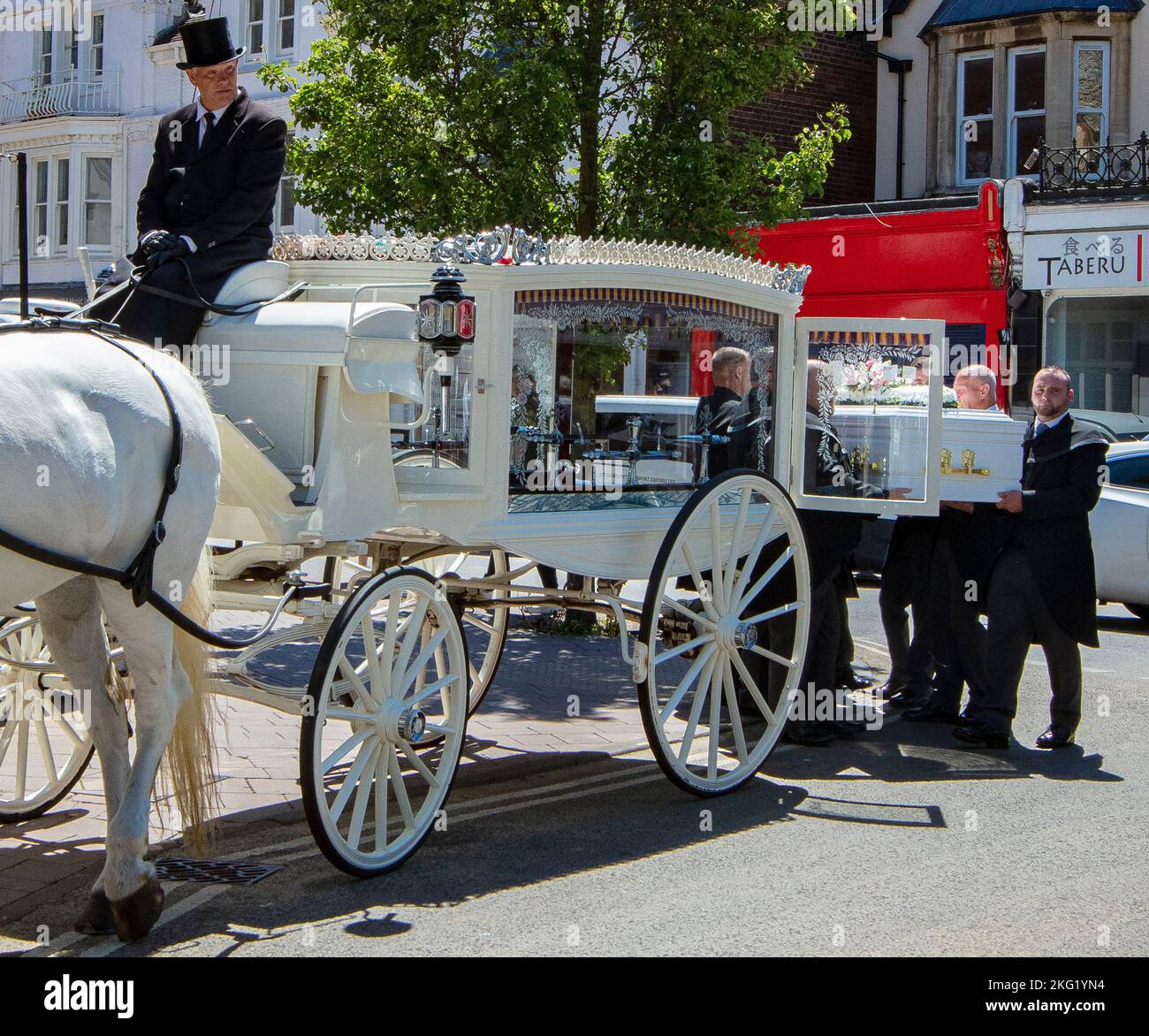 Corteo funerario vecchio stile sulla Cowley Road, Oxford; due grandi cavalli bianchi a pizzo disegnano un hearse bianco, con pallalori in nero Foto Stock