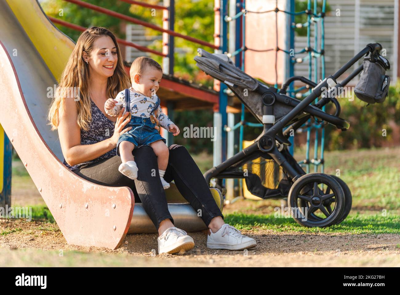 Madre con il suo bambino su uno scivolo del parco mentre il sole tramonta Foto Stock