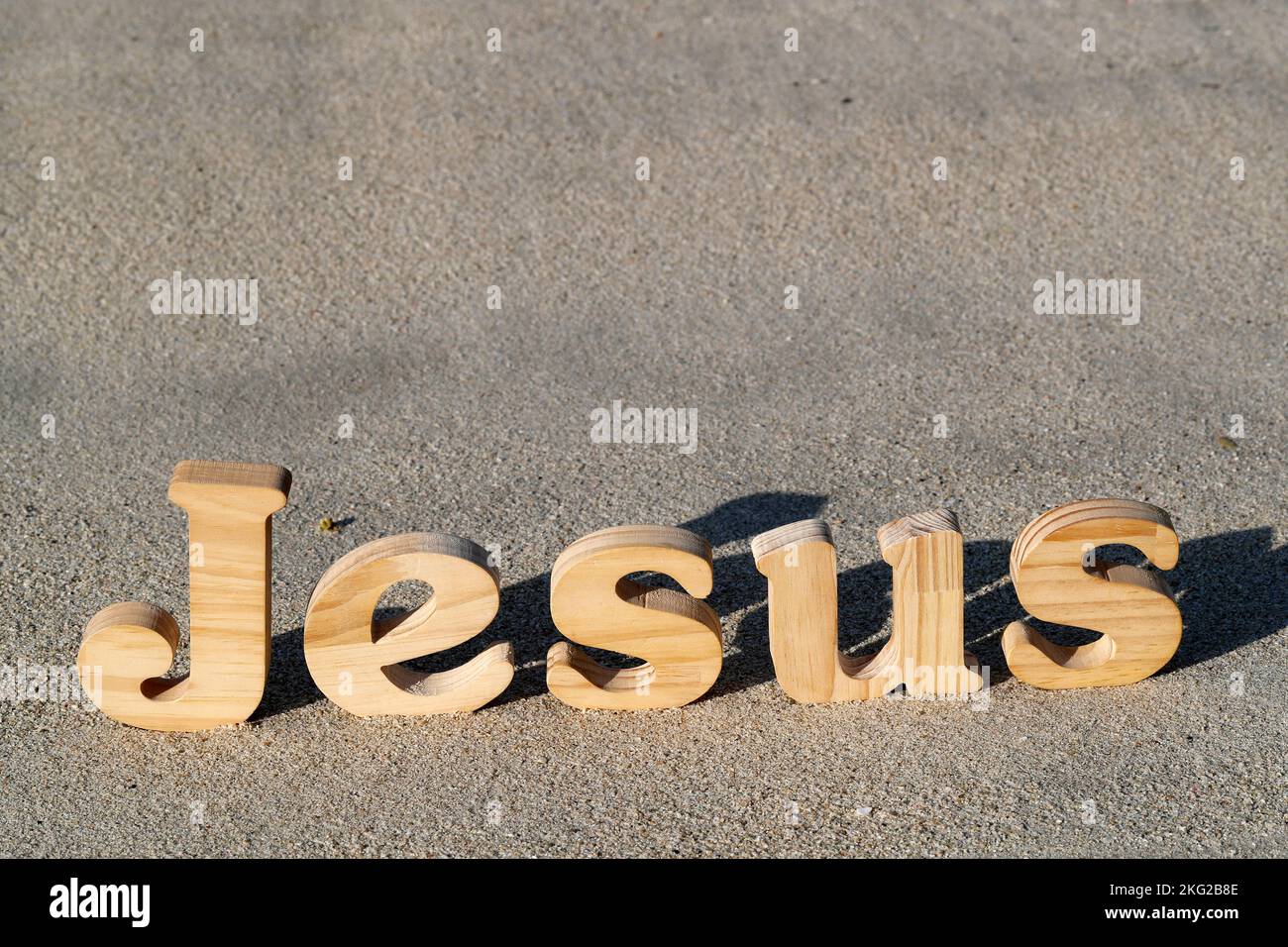 Lettere di legno che formano la parola Gesù con una Bibbia su uno sfondo di sabbia spiaggia. Simbolo del cristianesimo. Foto Stock