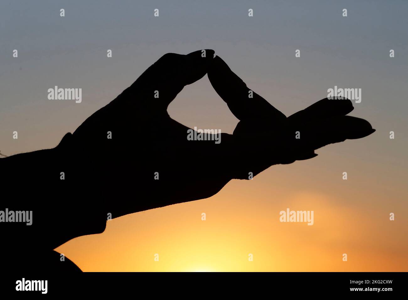 Donna che pratica yoga meditazione sul mare al tramonto come concetto di silenzio e relax. Primo piano a portata di mano, gyan mudra. Foto Stock