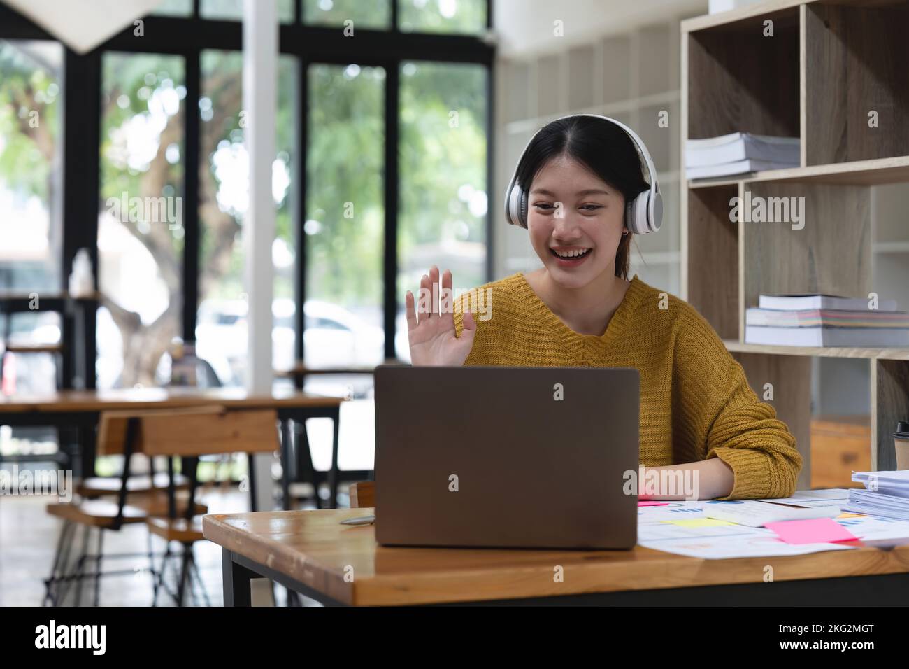 Amichevole donna asiatica tiene una riunione online mentre si siede a casa. Donna che sventolava la mano per salutare i partecipanti di una videochiamata. Formazione online Foto Stock