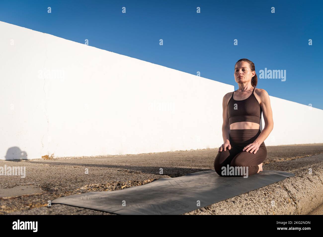 Donna che si inginocchiava sul suo materassino per esercizi al sole Foto Stock