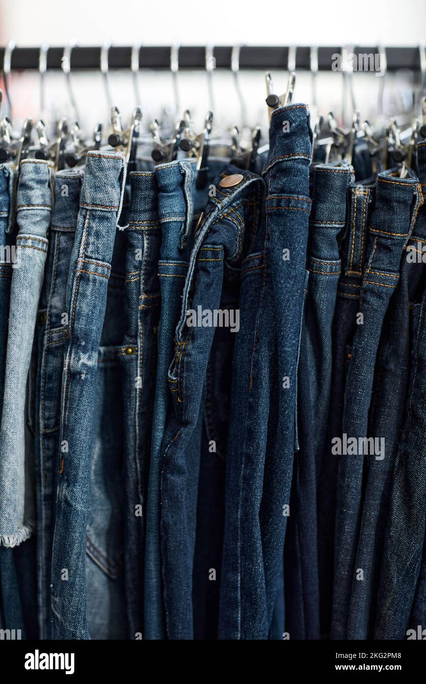 Immagine di sfondo verticale di jeans denim blu in fila sul rack di abbigliamento al negozio Thrift Foto Stock