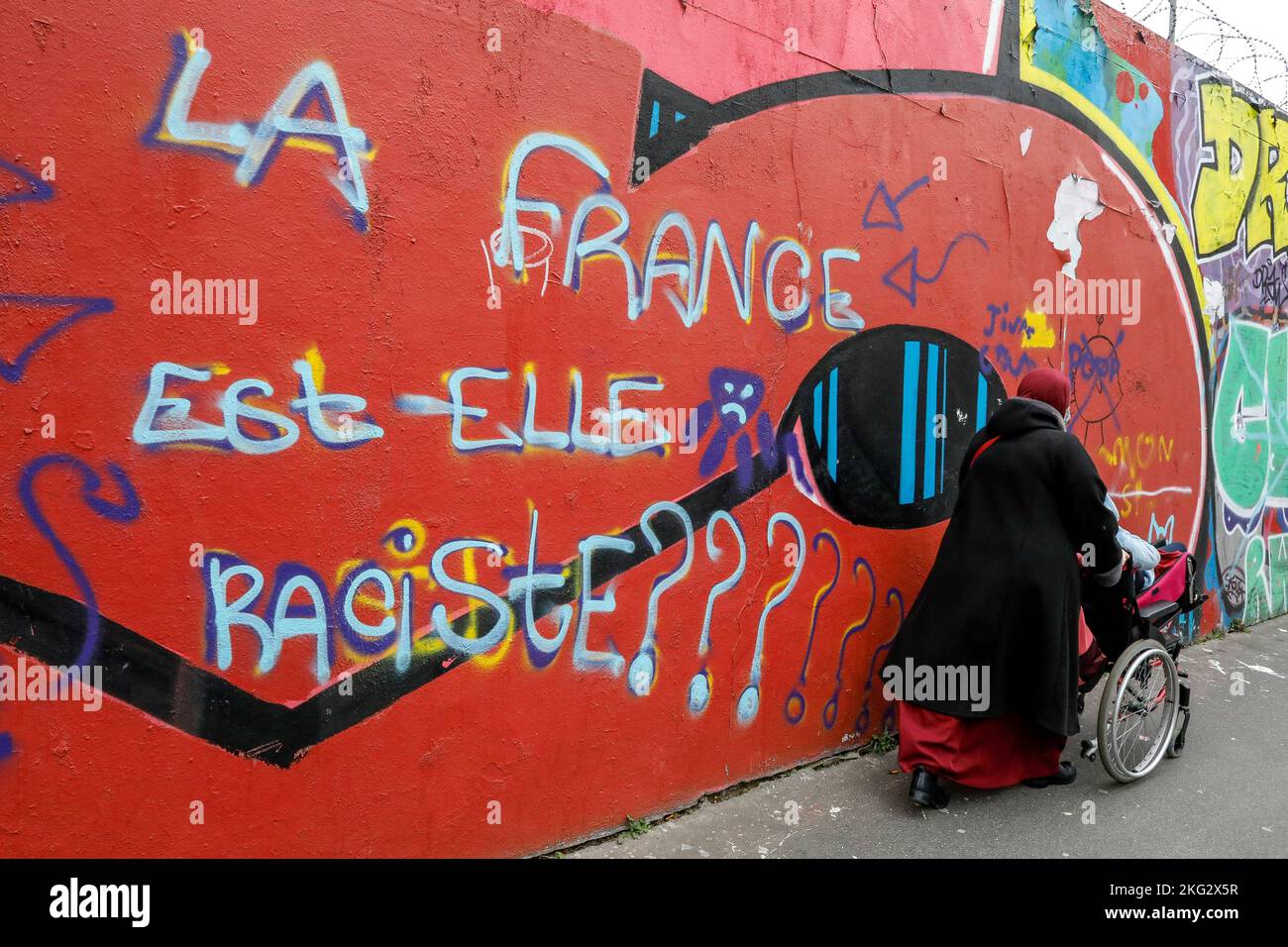Donna musulmana che passa davanti a un muro coperto di arte di strada a Parigi, Francia Foto Stock