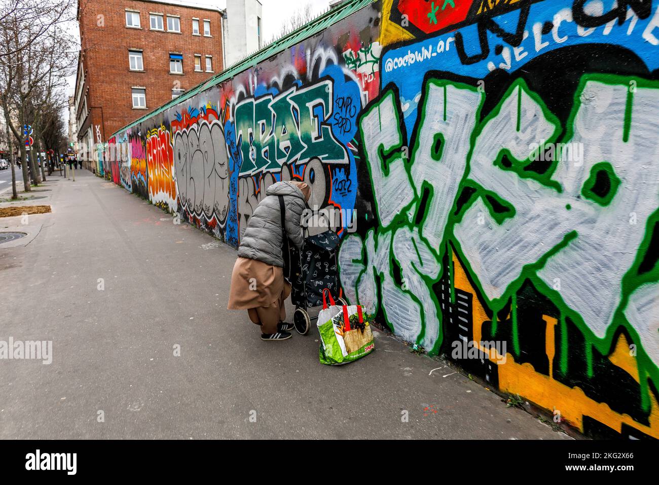 Donna che riposa accanto a un muro coperto di arte di strada a Parigi, Francia Foto Stock