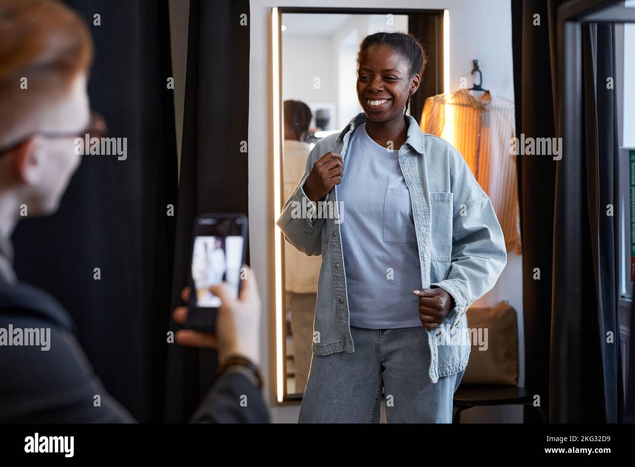Ritratto di una donna nera sorridente che indossa abiti in denim e posa per foto e video sul blog di moda sui social media Foto Stock