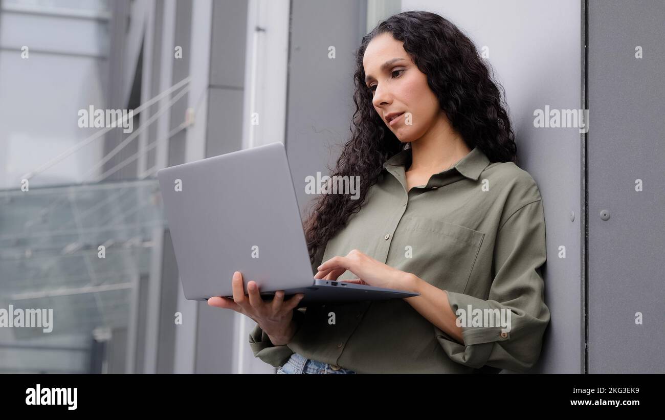 Serio 30s latino ispanica donna professionale businesswoman in piedi vicino ufficio edificio all'aperto parlando a distanza con connessione Wi-Fi videochiamata Foto Stock