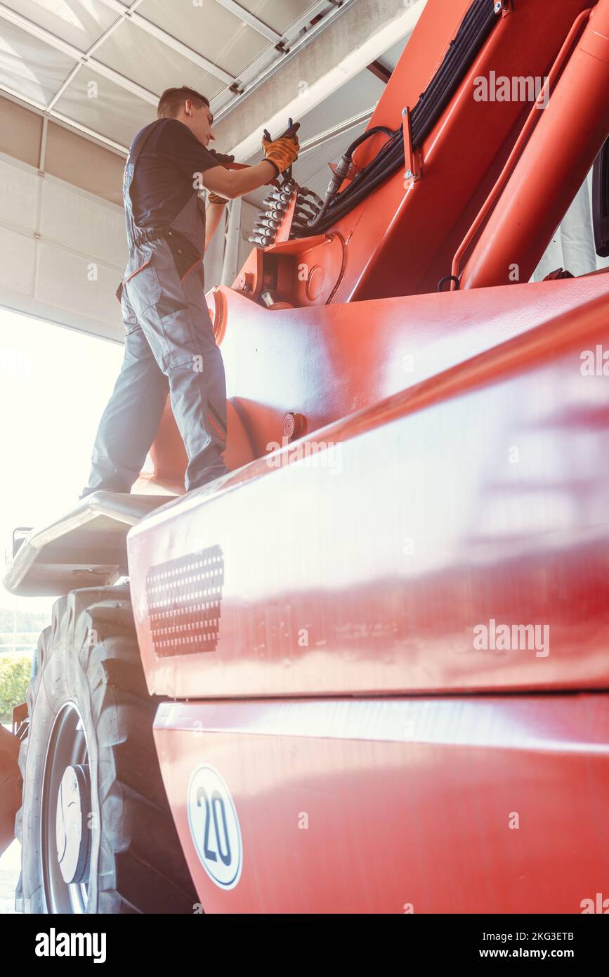 Machinista che ripara una macchina agricola enorme nel suo garage Foto Stock