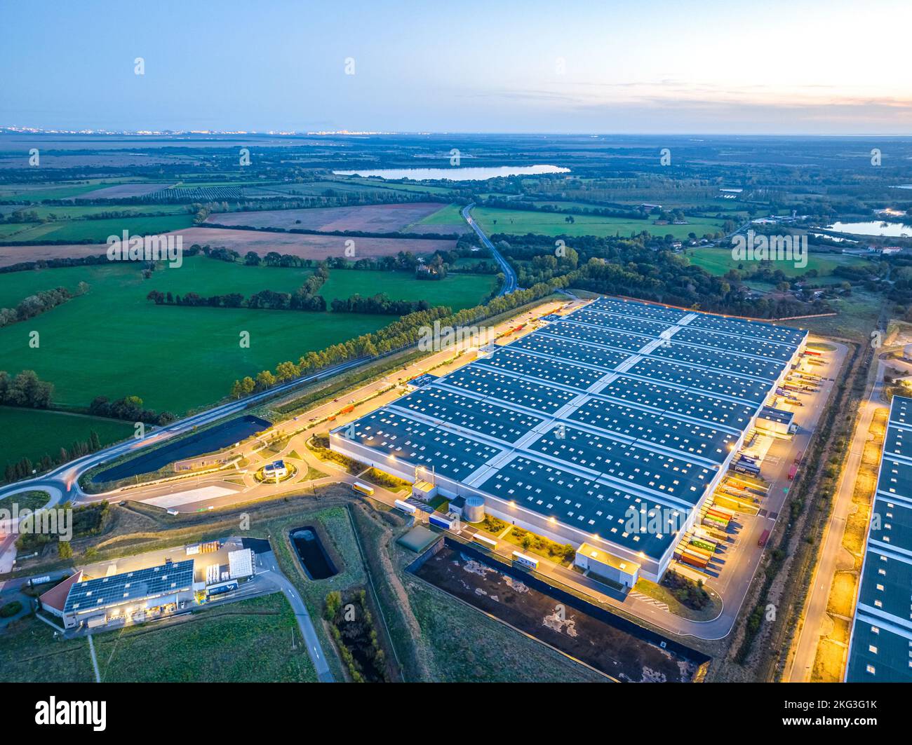 Foto drone di grande magazzino vicino alla superstrada circondata da vegetazione lussureggiante e camion parcheggiati nella baia di carico nella Val d'Oise, Francia Foto Stock