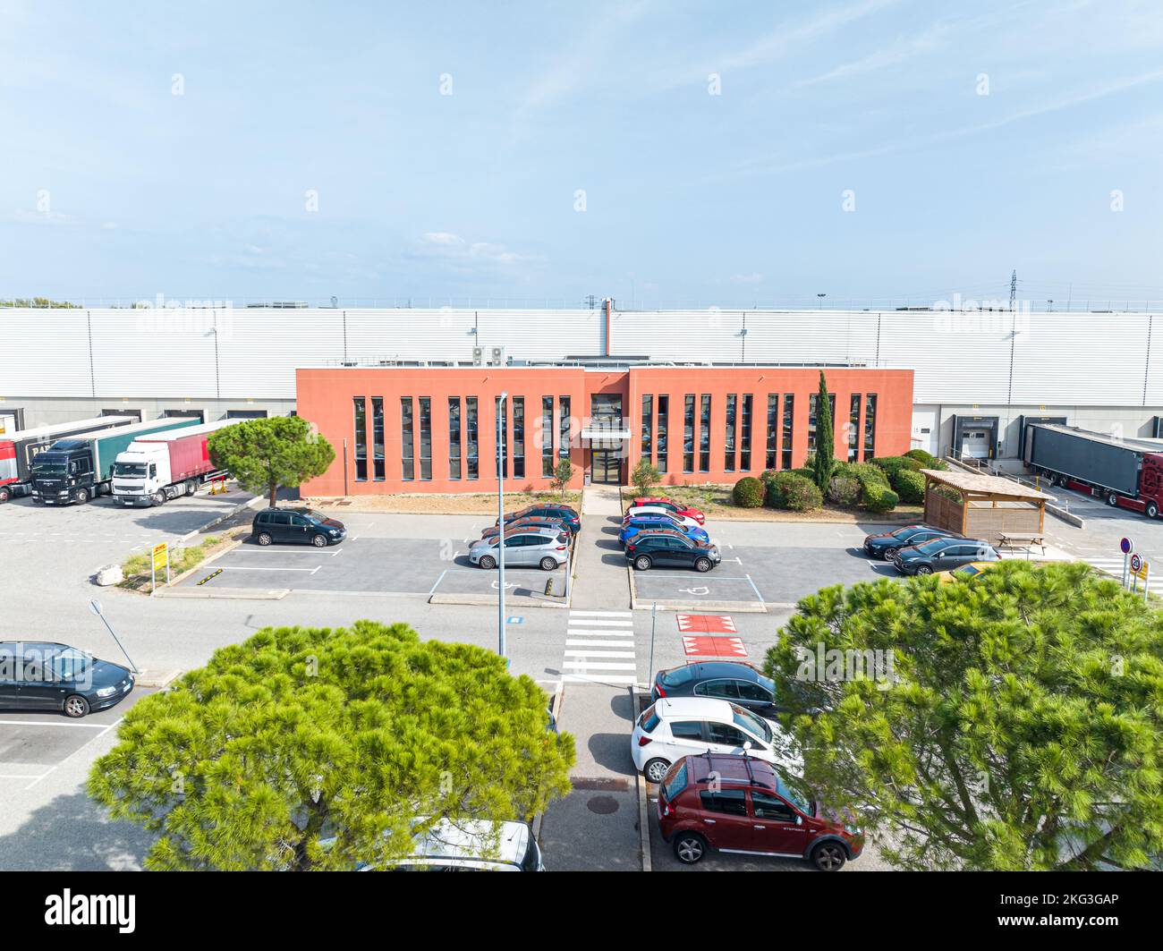 Vista aerea dell'ingresso anteriore dell'edificio degli uffici logistici con camion parcheggiati al banchina di carico con auto del personale in parcheggio Foto Stock