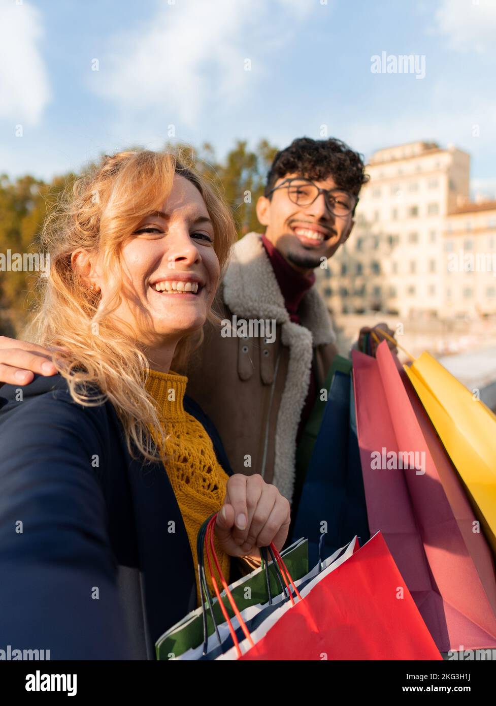 Felice coppia di amici che prendono un selfie in città tenendo borse per lo shopping in mano Foto Stock