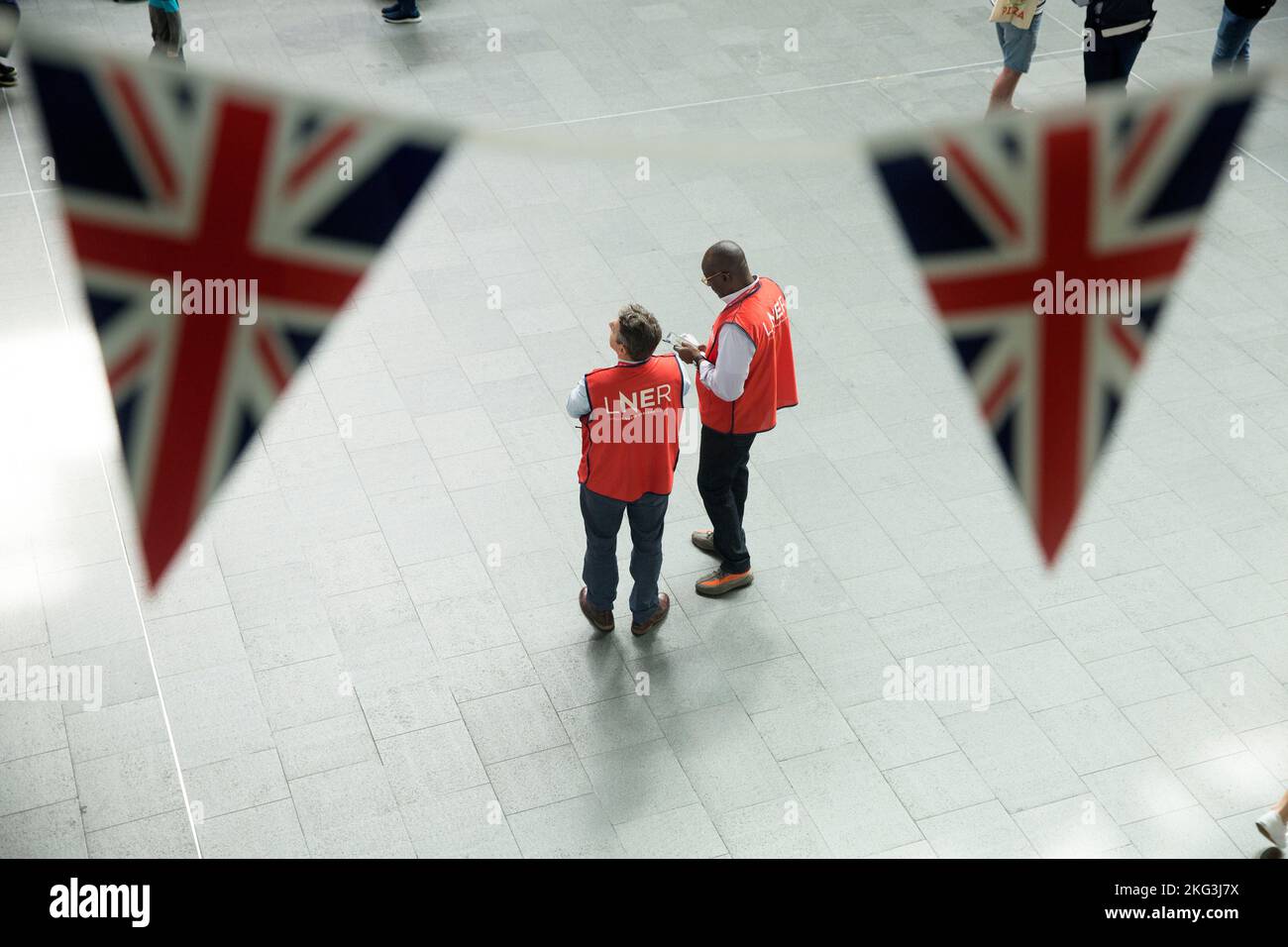 I membri del personale sono visti dietro un gruppo di bandiere dell’Unione mentre i passeggeri li oltrepassano alla King’s Cross Station di Londra il terzo giorno degli scioperi ferroviari. Foto Stock