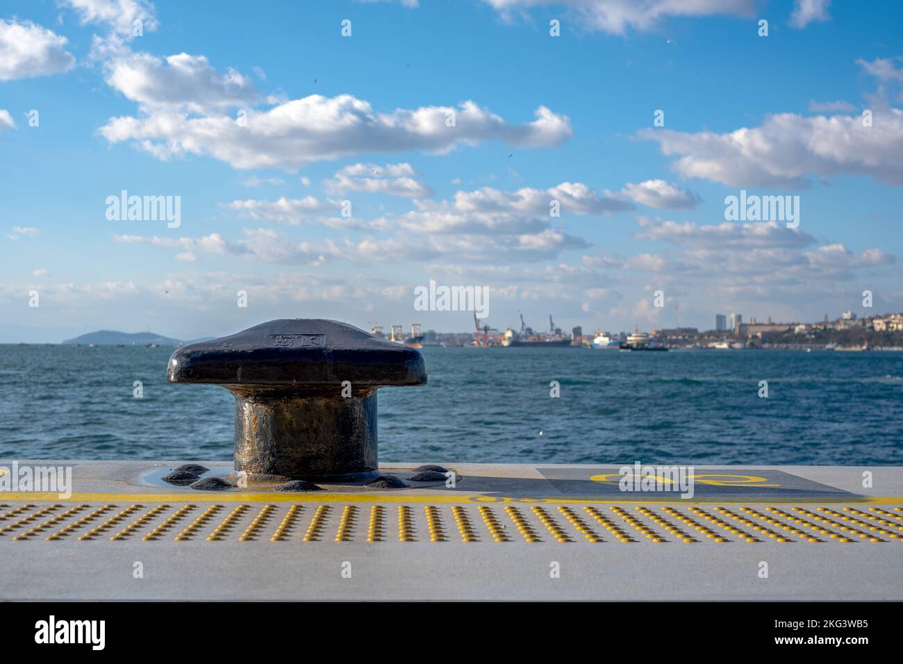 Paletto di ormeggio in metallo nero nella marina e nel terminal portuale. Paesaggio urbano di Noray sullo sfondo. Copia spazi. Foto Stock