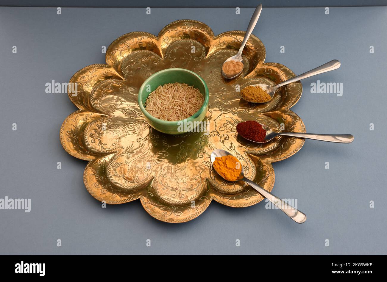Il riso in una ciotola di ceramica verde sedette su un antico vassoio indiano circondato da cucchiaini da tè contenenti peperoncino, curcuma, zenzero e curry in polvere a base blu Foto Stock