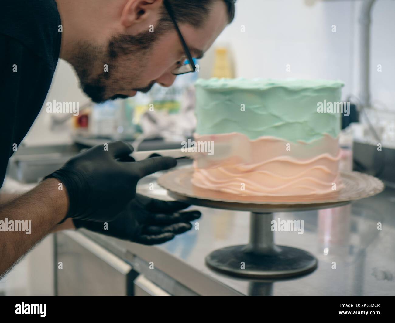 cake designer levigare una torta bianca ghiacciata con crema di burro turchese azzurro e rosa con spatola Foto Stock