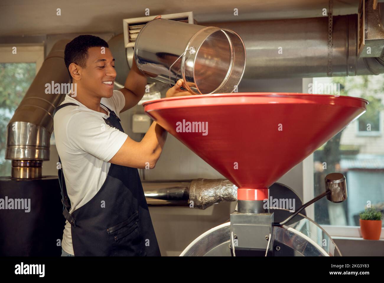 Lavoratore allegro versare i grani di caffè nella macchina di tostatura Foto Stock