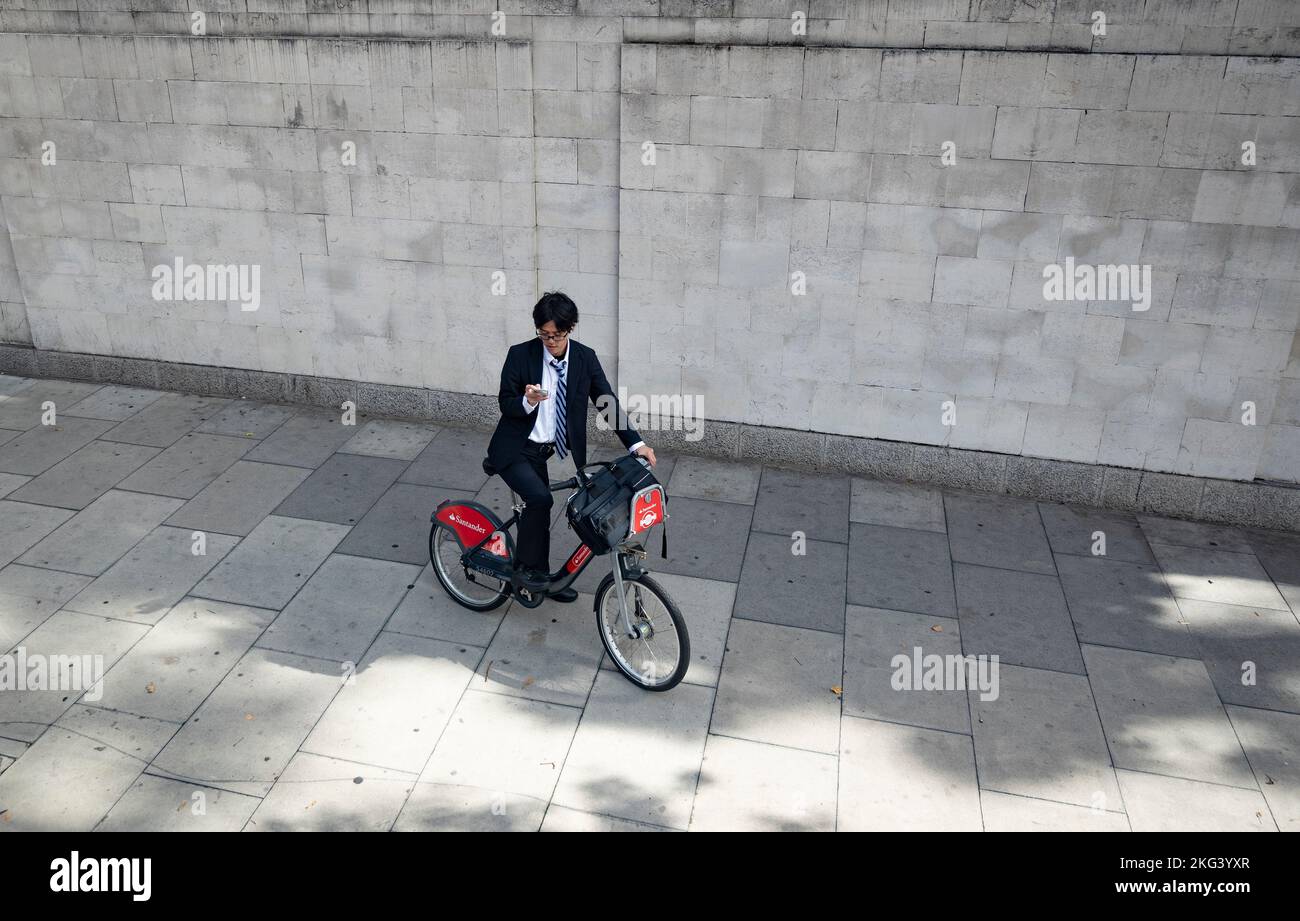 Giovane dirigente asiatico su una bicicletta pubblica con il suo smartphone Foto Stock