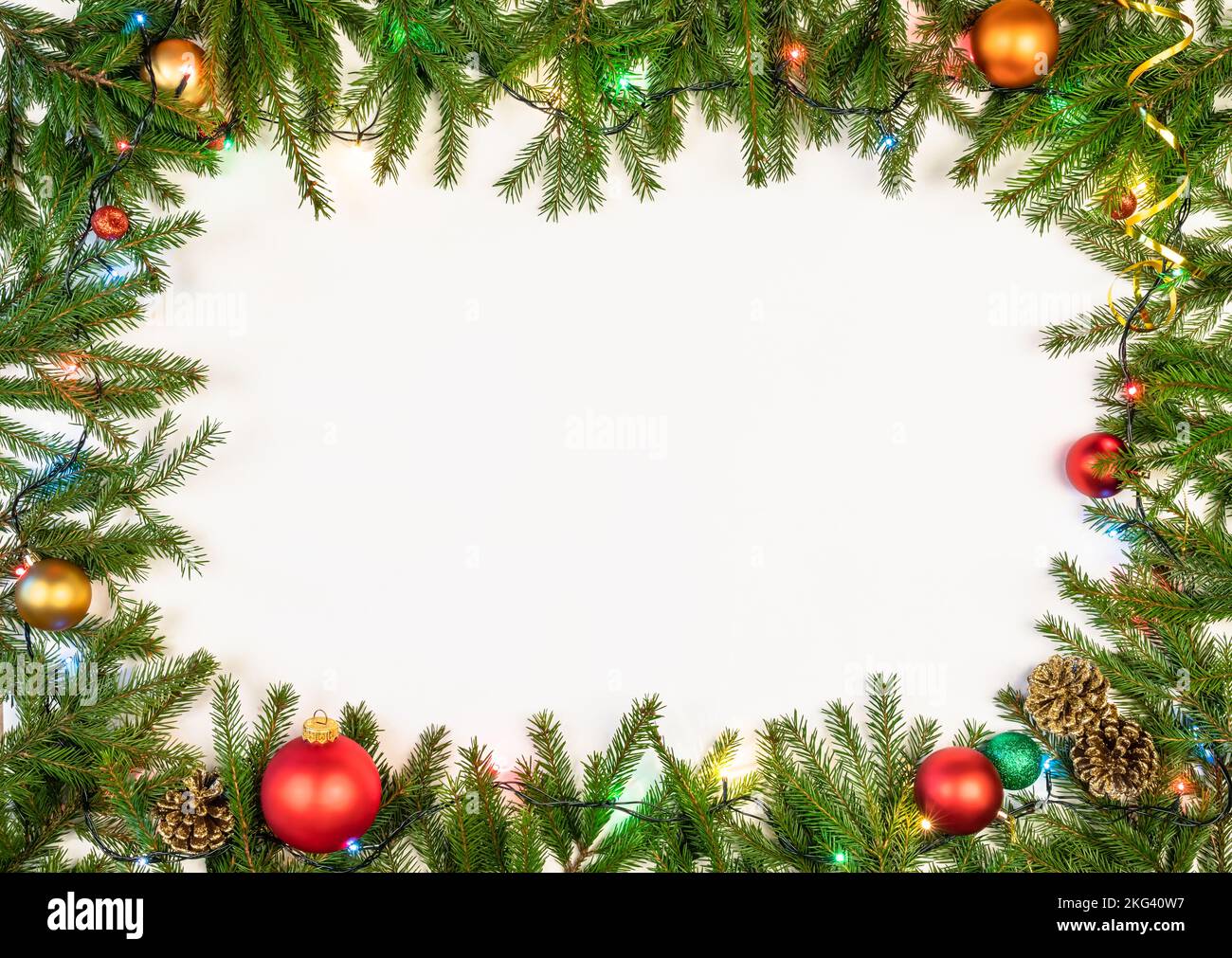 Cornice di Natale fatta di rami di abete baubles coni e luci elettriche multicolore di Natale su sfondo bianco Foto Stock