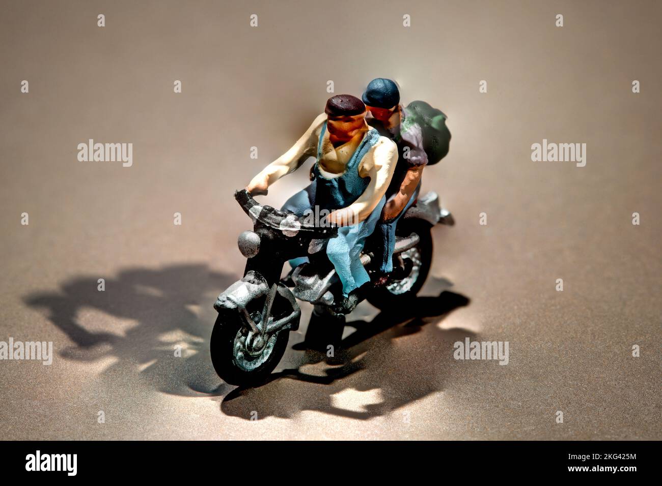 Uomini in miniatura che indossano zaini andare per un viaggio su una motocicletta su uno sfondo marrone con copyspace e ombre Foto Stock
