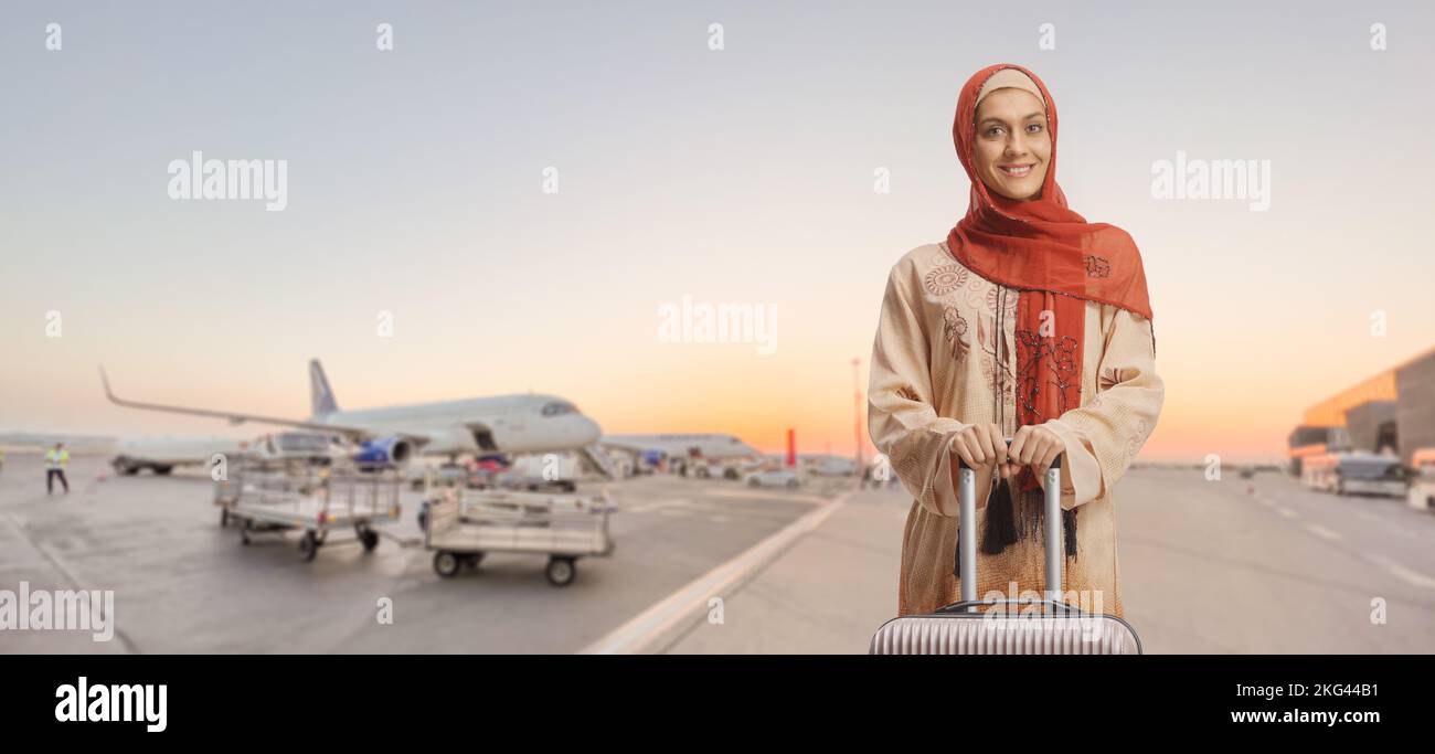 Donna in abiti etnici e hijab in piedi su un aeroporto con una valigia Foto Stock