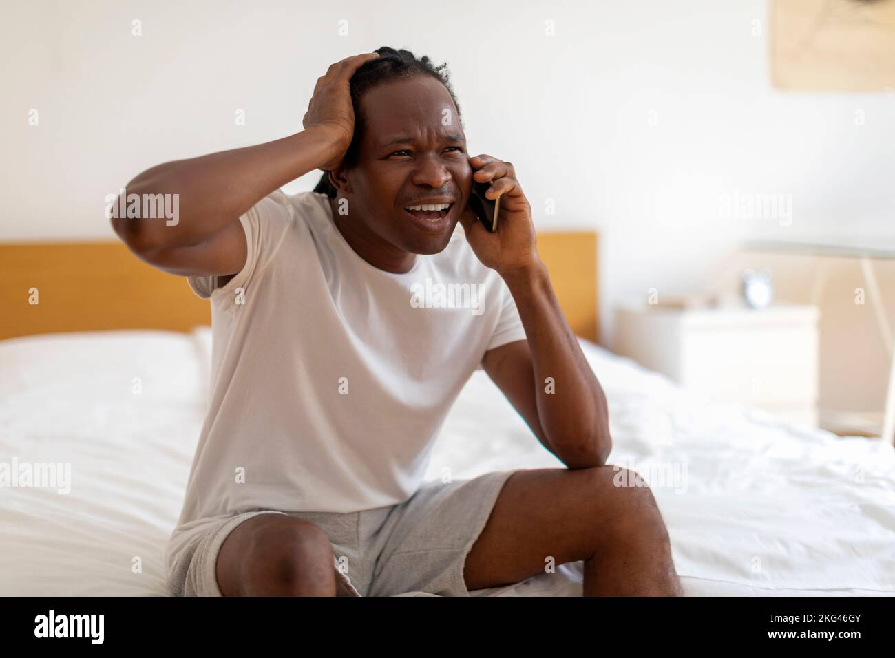 OH no Sottolinea l'uomo nero seduto sul letto e parlando sul cellulare Foto Stock
