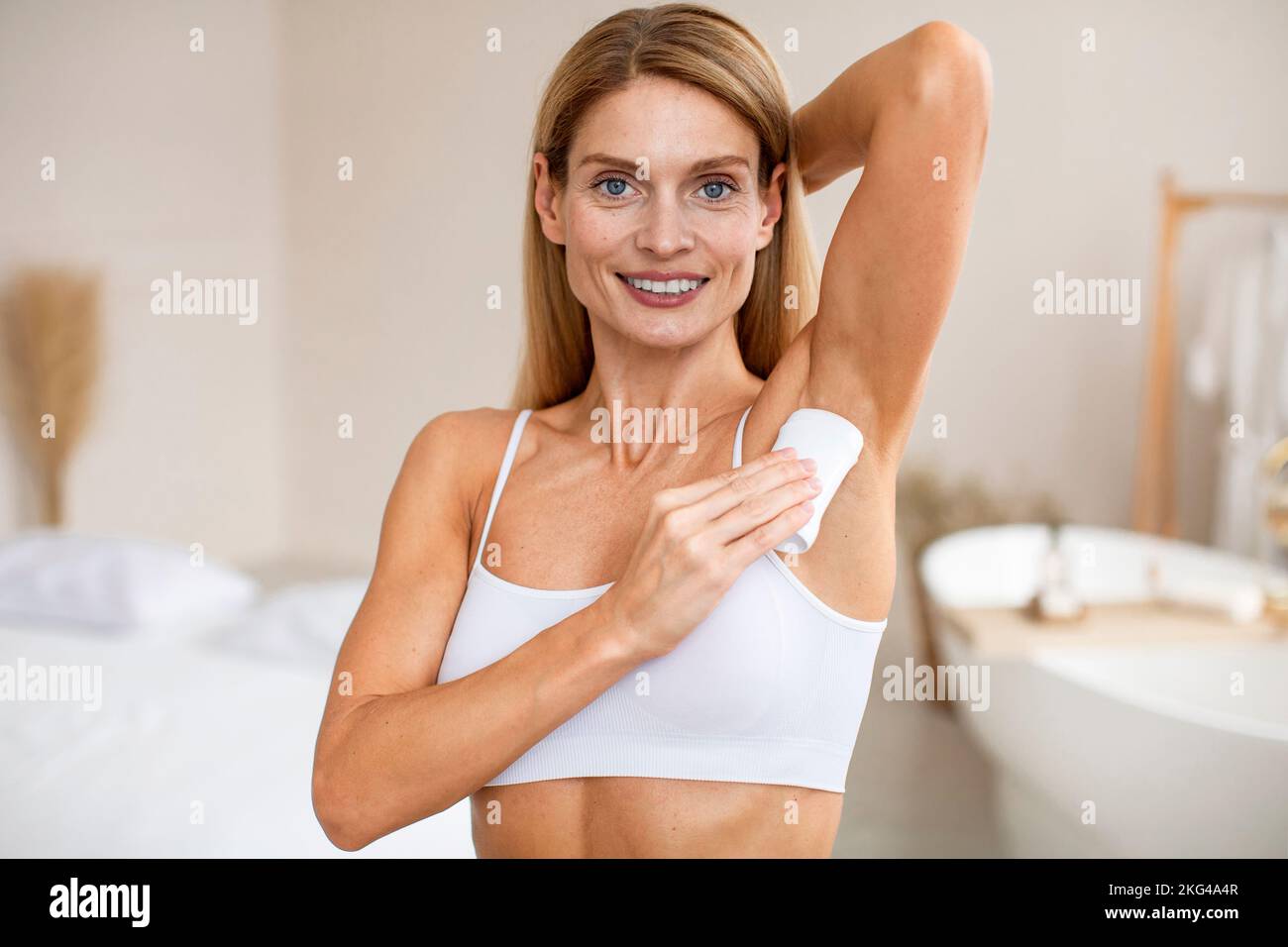 Ritratto di donna di mezza età positiva con bastone antitraspirante per ascelle, in piedi all'interno della stanza Foto Stock